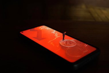 Üzerinde bitcoin resmi olan akıllı bir telefonun üzerinde duran bir iş adamı figürü.