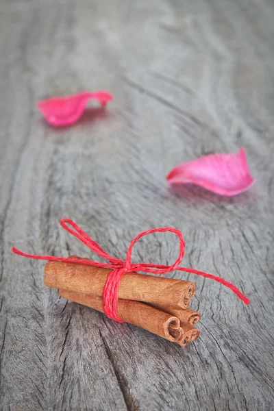 Canela stokken op de achtergrond roze bloemblaadjes op houten textuur. — Stockfoto