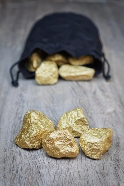 Goudklompjes verspreid stenen in een zak op een houten textuur. — Stockfoto