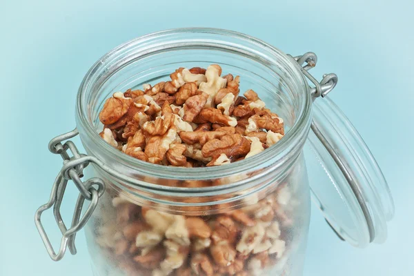 Peeled walnuts in a glass jar. On a blue background. — Stock Photo, Image