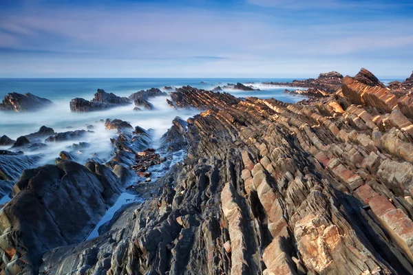 Ocean marine estran rocheux se lave avec un ciel bleu dramatique. — Photo