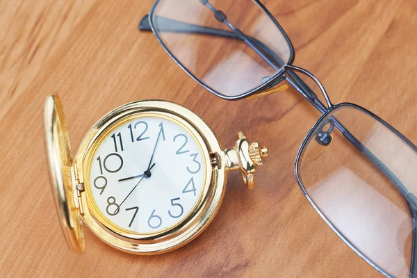Золотые карманные часы и очки на деревянные фоновой текстуры — стоковое фото