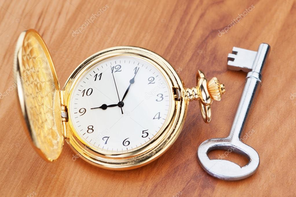 Gold pocket watch and key. Against the background of a wooden te