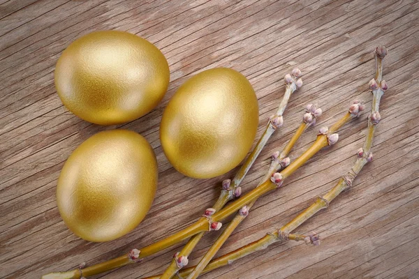Tři zlaté vejce a jarní větve na Velikonoce. na dřevěné textury — Stock fotografie