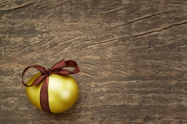 Huevo de Pascua oro con una cinta marrón, en una textura de madera. —  Fotos de Stock
