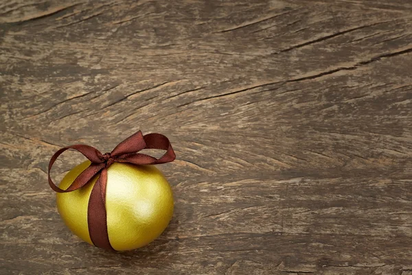 Easter golden egg with a brown ribbon, on a wooden texture. — Stock Photo, Image