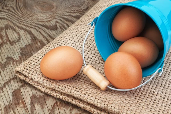 Blauwe emmer en Pasen eieren verspreid over rouwgewaad. — Stockfoto