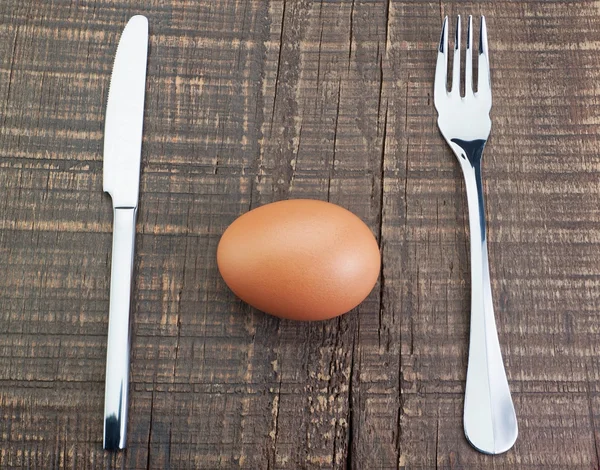 Cubiertos tenedor y cuchillo y huevo. en una textura de madera. — Foto de Stock