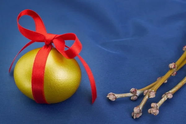 Mavi bir arka plan üzerinde kırmızı bir yay ile altın Paskalya yortusu yumurta. — Stok fotoğraf