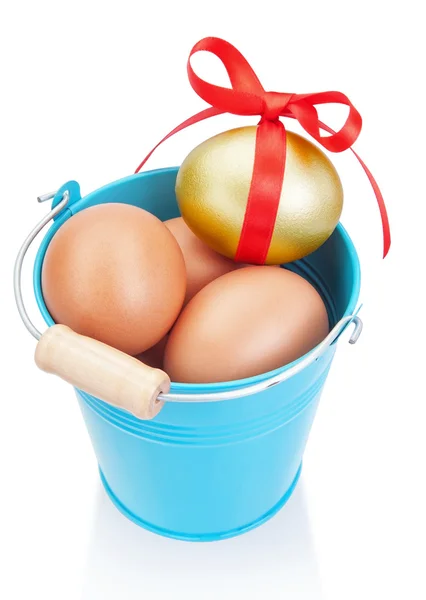 Uovo di Pasqua d'oro in un secchio blu. su uno sfondo bianco. — Foto Stock