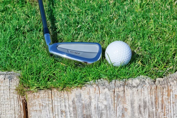 Golfbal en stok omgekeerde houten ondersteuning op het gras. — Stockfoto