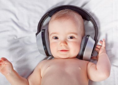 Cute baby listens to music through headphones. Close-up. clipart