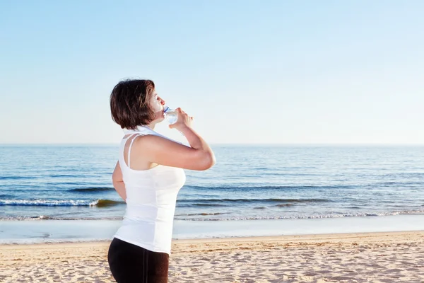 La chica en la playa después de ejercicio beber, agua. con una toalla. —  Fotos de Stock