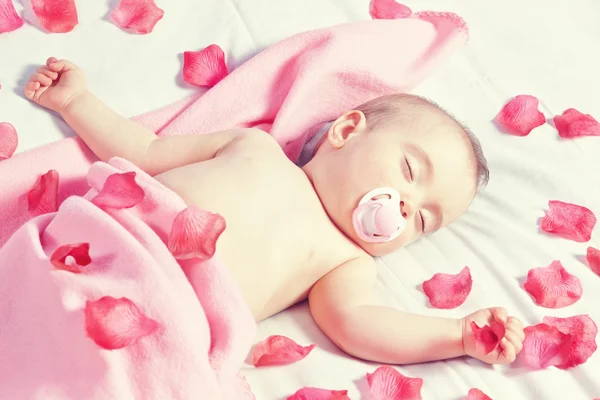 Barn tjej sova i en säng beströdd med rosenblad in. i th — Stockfoto