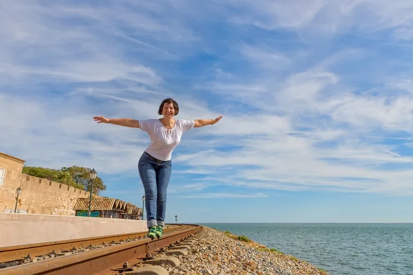 Chica feliz caminar sobre los rieles y sonriendo. en el fondo del mar azul. — Foto de Stock