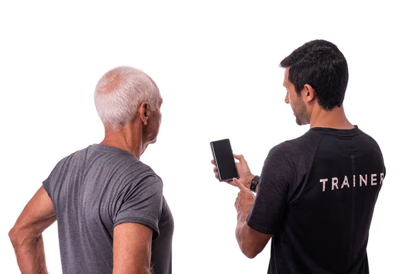 Fitness trainer spiega ad un uomo anziano come utilizzare un'applicazione software per l'allenamento su uno sfondo bianco isolato. Copia spazio — Foto Stock