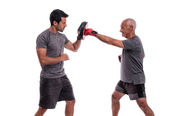 Elderly man hits with boxing glove in defense, personal fitness trainer, concept of working together. On white background. — Stock Photo, Image