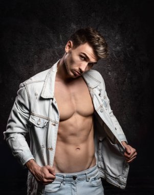 Avrupalı atletik genç adam, dış giysisiz poz veriyor, spor fiziki formda. Koyu dokulu bir arka planda. Ceket omuzda..