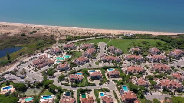 Flygöversikt över Quinta do Lago semesteranläggningar i Vale de Lobo, Algarve, Portugal, Europa. Skott av hustak av lyxstugor i grönt landskap med berg på bakgrunden. Golfplaner. — Stockvideo