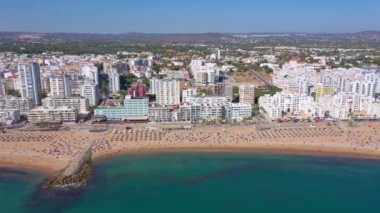 İnsansız hava aracı görüntüleri, Atlantik Okyanusu kıyısında turist kasabası Quareira 'yı çekiyor, turistlerle dolu plajlar. Portekiz, Algarve.