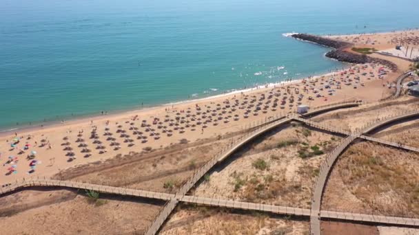 Drone vlucht over de stranden en houten paden van de Portugese stad Quarteira, met toeristen op ligstoelen. Portugal Algarve. — Stockvideo