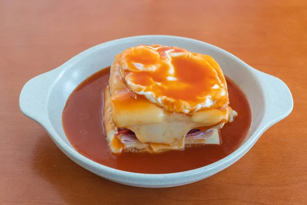 Sandwich-ul fierbinte Francesinha cu cârnați și carne, brânză topită, turnată cu sos de bere și acoperită cu un ou prăjit. Închideți într-o farfurie pe masă. — Fotografie, imagine de stoc