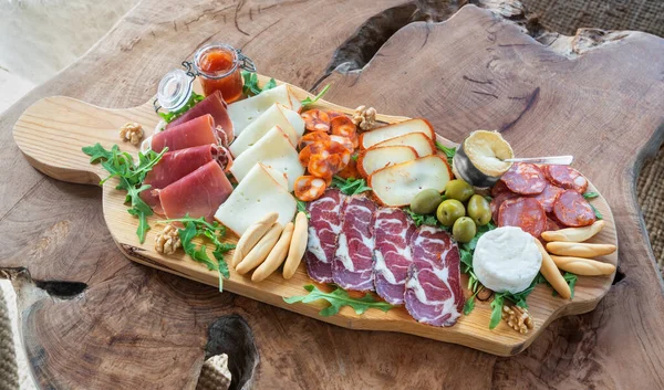 Very colorful tapas board of charcuterie with cheese and smoked meats. Decorated with arugula and walnuts. Wine snacks. On a decorative table. — Stock Photo, Image