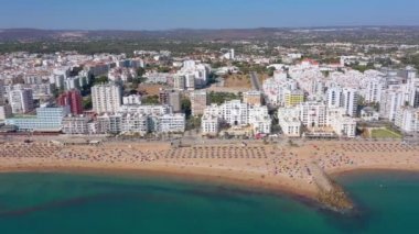 İnsansız hava aracı görüntüleri, Atlantik Okyanusu kıyısında turist kasabası Quareira 'yı çekiyor, turistlerle dolu plajlar. Portekiz, Algarve.