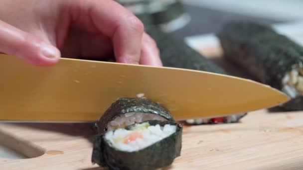 El chef corta sushi y rollos hechos de mariscos con ingredientes asiáticos con un cuchillo. Primer plano, macro. El fondo está borroso. Movimiento lento — Vídeo de stock