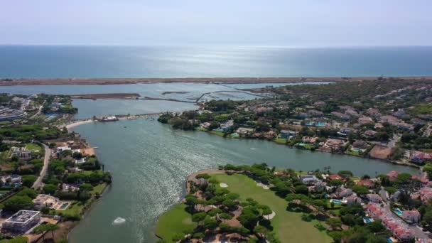 Aerial overview of Quinta do Lago resort buildings in Vale de Lobo, Algarve, Portugal, Europe. Shot of rooftops of luxury cottages in green landscape with mountains on background. Golf fields. — Stock Video