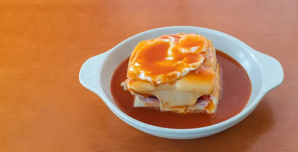 Горячий сэндвич Франчесинья с сосисками и мясом, плавленный сыр, наливаемый пивным соусом и увенчанный жареным яйцом. Закрыть в тарелку на столе. — стоковое фото