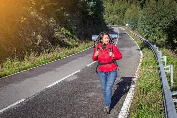 Una turista donna, in giacca, in autostop sulla strada, cammina lungo le strade forestali portoghesi. Ferma i compagni di viaggio. Giornata di sole. — Foto Stock