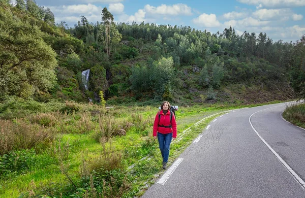 ジャケットを着た女性観光客が道をヒッチハイクしてポルトガルの森林道を歩いている。仲間の旅行者を止める. — ストック写真