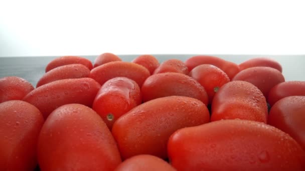 Zralá červená biologická rajčata v řadě na hladkém skleněném povrchu. Posuneme se dopředu, dozadu. Extremní makro. — Stock video