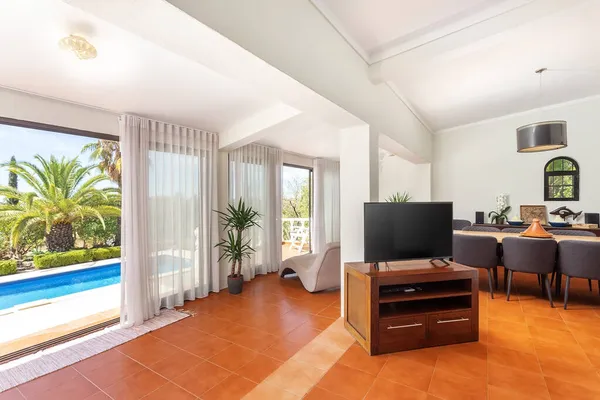 Moderne traditionele Europese woonkamer met TV eettafel met uitzicht op het zwembad en de tuin met palmbomen. — Stockfoto