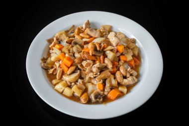 Geleneksel Çin usulü tavuk güveci, badem, havuç ve makarna. Siyah arkaplanda bir plakada, yakın plan..