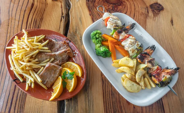 Brocheta de mariscos a la parrilla hecha de camarones, pescado y pimientos con papas fritas, zanahorias y brócoli, naranja, en el lateral. Sobre una superficie de madera. —  Fotos de Stock