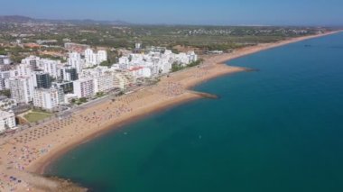 İnsansız hava aracı görüntüleri, Atlantik Okyanusu kıyısında turist kasabası Quareira 'yı çekiyor, turistlerle dolu plajlar. Portekiz, Algarve.