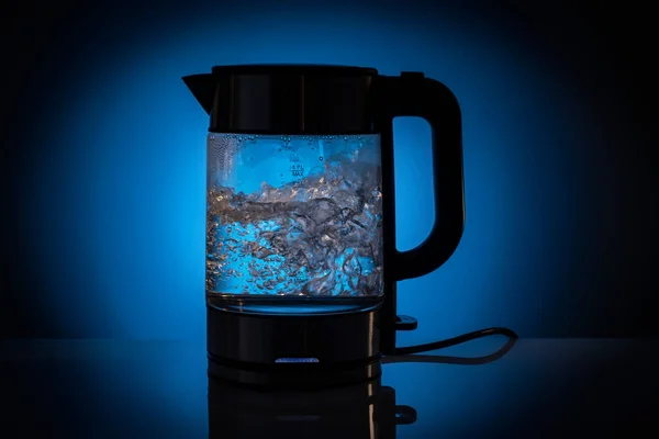 Hervidor eléctrico de vidrio lleno de agua mientras hierve. Sobre un fondo conceptual azul. —  Fotos de Stock