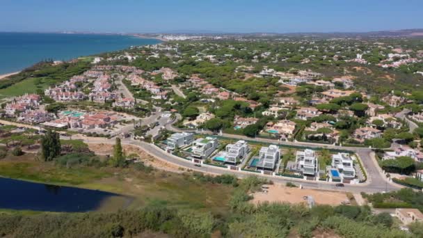 Flygöversikt över Quinta do Lago semesteranläggningar i Vale de Lobo, Algarve, Portugal, Europa. Skott av hustak av lyxstugor i grönt landskap med berg på bakgrunden. Golfplaner. — Stockvideo