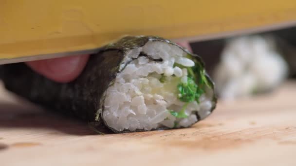 El chef corta sushi y rollos hechos de mariscos con ingredientes asiáticos con un cuchillo. Primer plano, macro. El fondo está borroso. Movimiento lento — Vídeo de stock