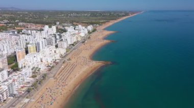 İnsansız hava aracı görüntüleri, Atlantik Okyanusu kıyısında turist kasabası Quareira 'yı çekiyor, turistlerle dolu plajlar. Portekiz, Algarve.