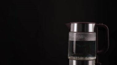 El, kaynar su, içecek, çay ya da kahve için bir bardak elektrikli su ısıtıcısı alır. Siyah bir arkaplanda.
