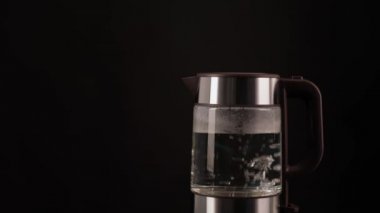 El, kaynar su, içecek, çay ya da kahve için bir bardak elektrikli su ısıtıcısı alır. Siyah bir arkaplanda.