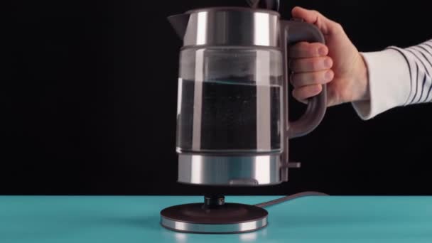 La mano prende un bollitore elettrico di vetro per l'acqua bollente, per bevande, tè o caffè. Su uno sfondo nero. — Video Stock