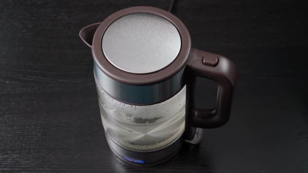 Ręka bierze szklaną czajnik elektryczny do gotowania wody, do napojów, herbaty lub kawy. Na czarnym tle. — Wideo stockowe