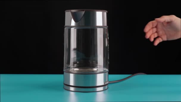 The hand takes a glass electric kettle for boiling water, for drinks, tea or coffee. On a black background. — Stock Video