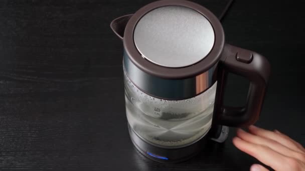 La mano toma un hervidor eléctrico de vidrio para hervir agua, para bebidas, té o café. Sobre un fondo negro. — Vídeo de stock
