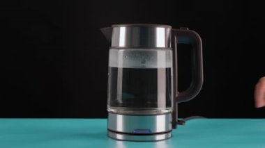 El, kaynar su, içecek, çay ya da kahve için bir bardak elektrikli su ısıtıcısı alır. Siyah bir arkaplanda.