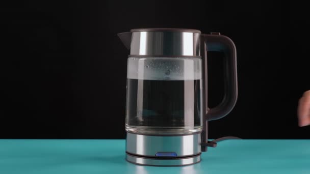 La mano prende un bollitore elettrico di vetro per l'acqua bollente, per bevande, tè o caffè. Su uno sfondo nero. — Video Stock